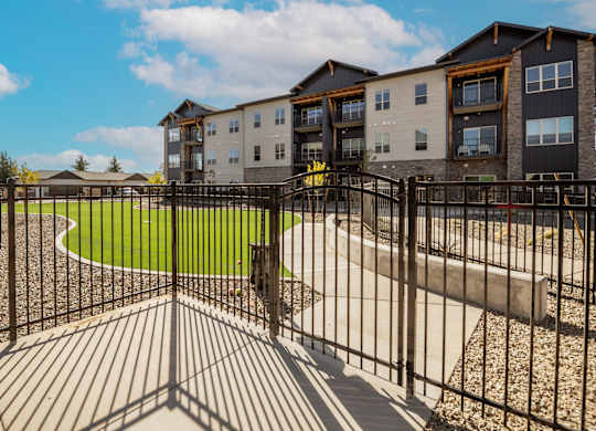 A black metal fence surrounds a playground area in front of apartment buildings.
