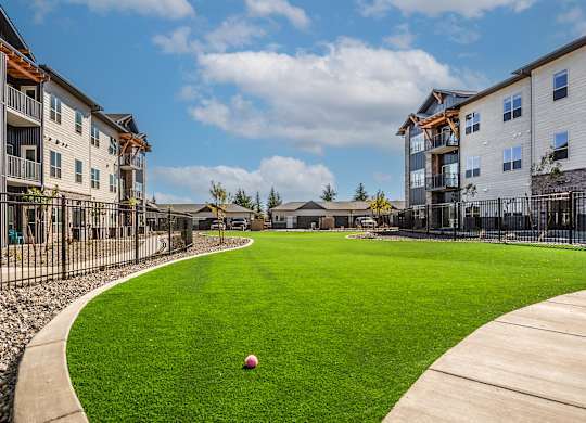A ball is sitting on a green lawn in front of apartment buildings.