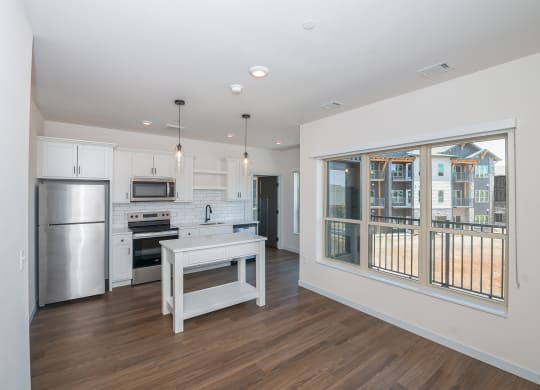 a living room with a large window and a kitchen with stainless steel appliances at The Crossings  at Windsong, Prescott Valley, 86314