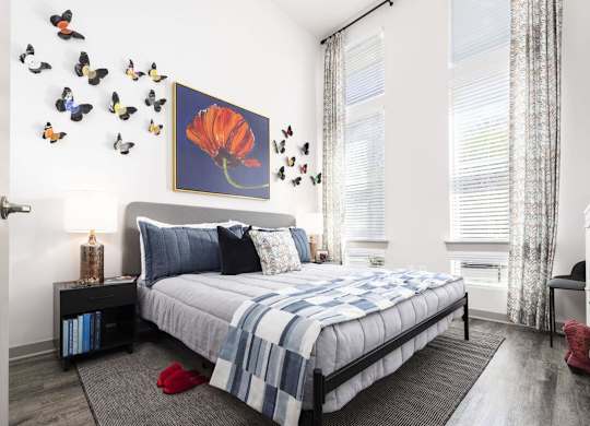 A bedroom with a bed, a painting of a flower, and butterflies on the wall.