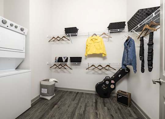 A room with a guitar and clothes hanging on the wall.