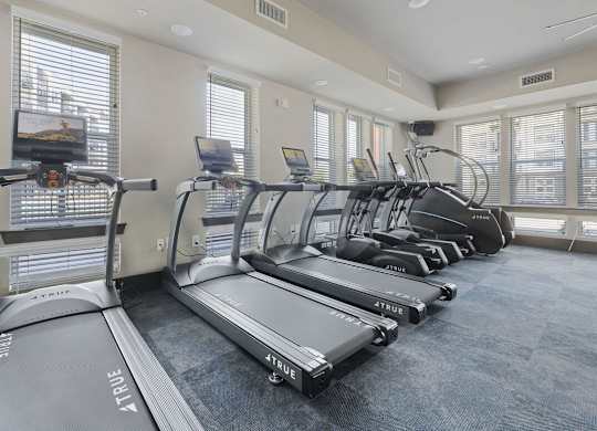 A row of treadmills in a gym with a television on the wall.