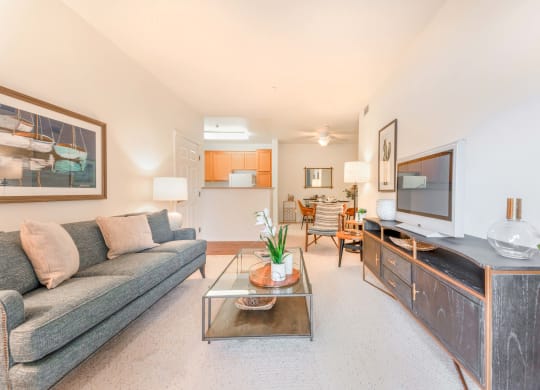 Goleta Apartments- Sumida Gardens- Living Room with Plush Carpeting, a Grey Couch, and Glass Coffee Table