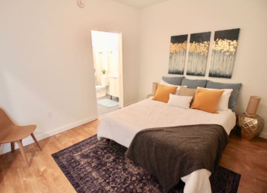 A bedroom with a bed, chair, and artwork on the wall.
