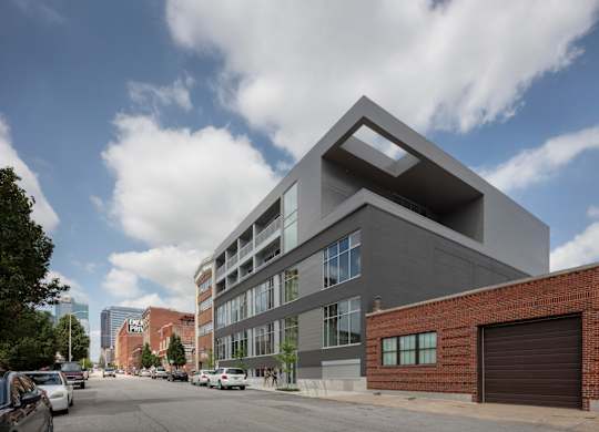 A modern building with a unique design is situated on a street with cars parked on the side.