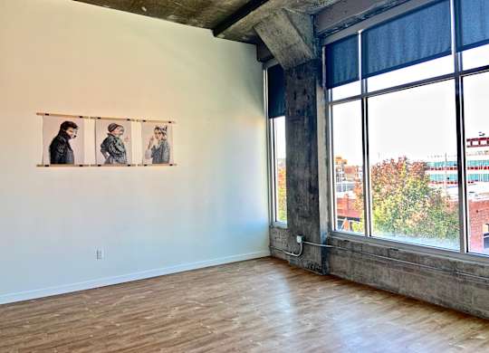 Three people are standing in front of a window in a room with wooden floors.