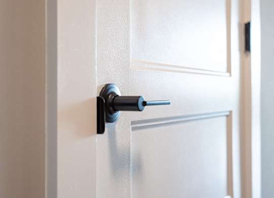 A door handle with a keyhole is on a white door.