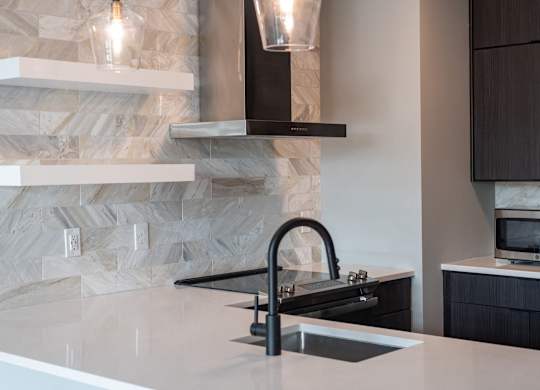 A modern kitchen with a stone backsplash and a black faucet.
