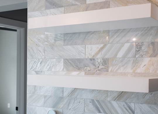 A marble wall with a white shelf above it.