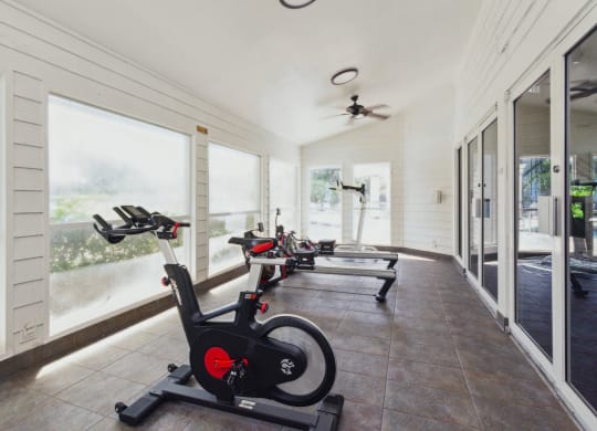 a row of exercise bikes in a room with windows at The Villages of Banyan Grove, Florida, 33436