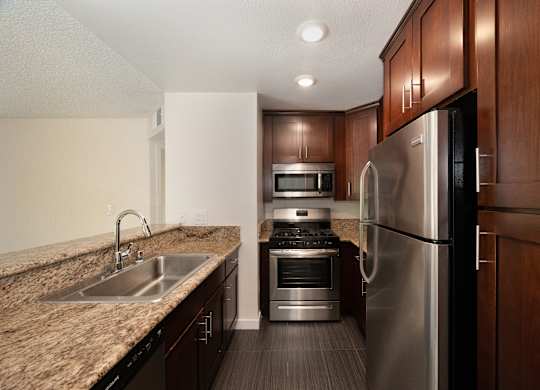 a kitchen with dark wood cabinets and granite countertops and stainless steel appliances at Croft Plaza Apartments, West Hollywood, CA