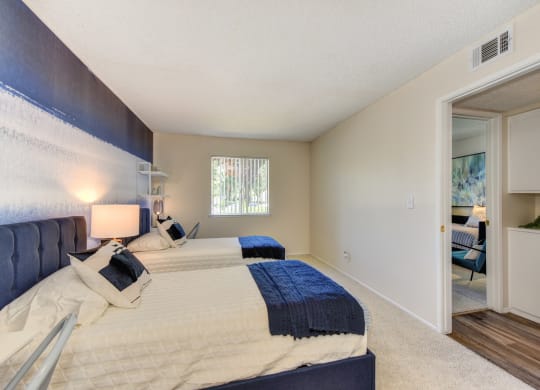 Bedroom with 2 twin beds with blue and white bedding.  Washer and dryer visible in hallway at Renaissance Park Apartments, Davis, California