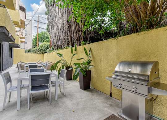 Community BBQ Area with Grill, Picnic Tables, Yellow Wall and Cement Floor at Croft Plaza Apartments, West Hollywood, 90069