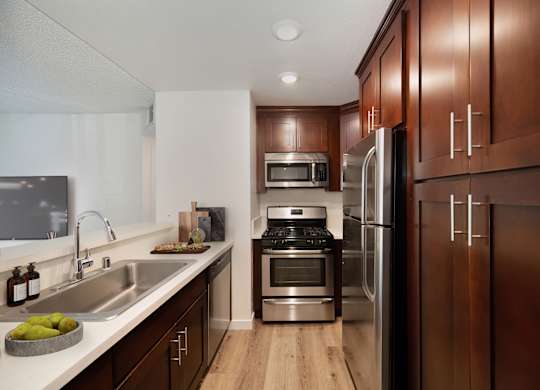 a kitchen with wooden cabinets and stainless steel appliances at Croft Plaza Apartments, West Hollywood California