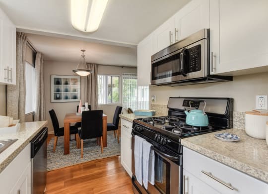 Dining Room/Kitchen with Wood Inspired Floor, Rug, Oven, Stove with Blue Tea Kettle, Microwave, Wood Dining Room Table and Chairs at Addison Ranch Apartments, Petaluma, 94954