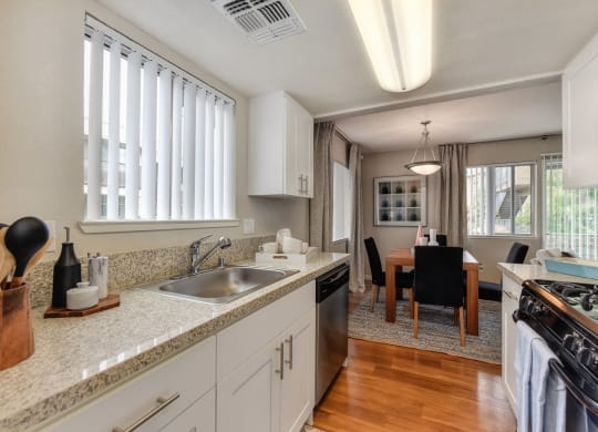 Kitchen with View of Dining Room with Wood Inspired Floor, Sink, Cupboards, Stove, Oven, Wooden Dining Room Table and Black Chairs at Addison Ranch Apartments, Petaluma, CA