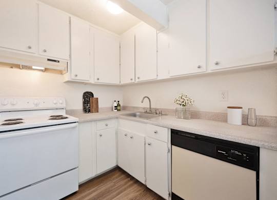 A white kitchen with a stove, sink, and cabinets.