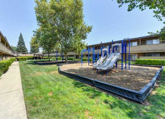 Community Outdoor Playground with Slides, Woodchip Floor and Grass  at Olympus Park Apartments, Roseville, CA, 95661