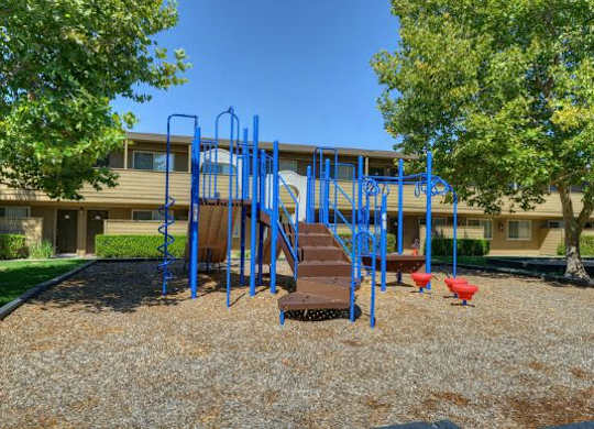Outdoor Playground with Jungle Gym, Wood Chip Ground, Grass and Trees  at Olympus Park Apartments, Roseville, CA
