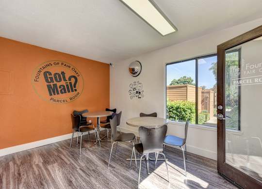 Parcel Room with Hardwood Inspired Floor, Short Round Tables, Chairs, Orange Wall with at Fountains of Fair Oaks, Fair Oaks
