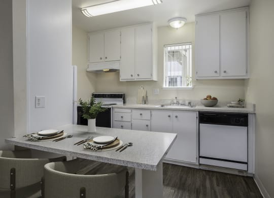 a kitchen with white cabinets and a table and chairs at Renaissance Park Apartments, California