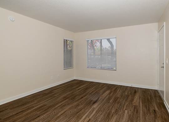 A room with wooden flooring and two windows with blinds.