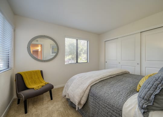 Master Bedroom with gray comforter. Room has Carpet, Gray Chair in corner, large closet with 3 doors and Window at Rocklin Manor  Apartments, California