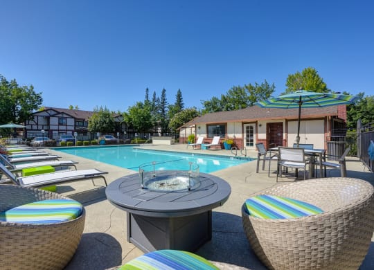 Swimming pool area with chaise lounge chairs, umbrellas, tables and gas firepit at Rocklin Manor  Apartments, Rocklin  , California