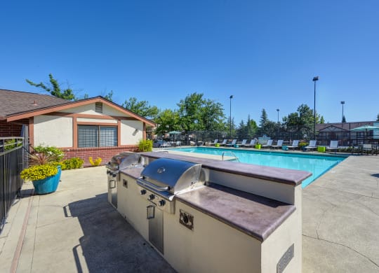 BBQ and Seating Area with Grills, Table, Blue/Yellow Patio Umbrella, Lime Green Chairs and View of Pool at Rocklin Manor  Apartments, Rocklin  