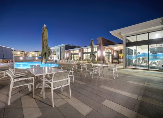 The swimming pool lounge area with tables, chairs and umbrellas at night.