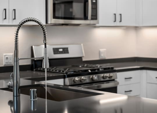 a kitchen with a sink with a gooseneck style faucet with water turned on and a stove in the distance