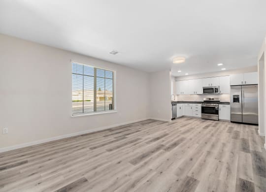 an empty living room and kitchen with wood flooring and a window