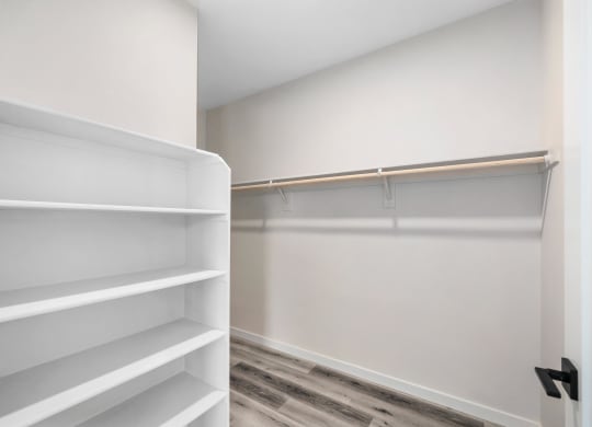 a walk in closet with white shelves and a wood floor