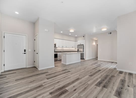 an empty living room and kitchen with white walls and wood flooring