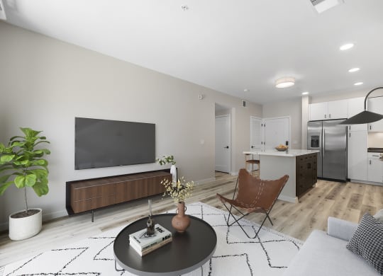 a living room with a tv on the wall and a kitchen in the background