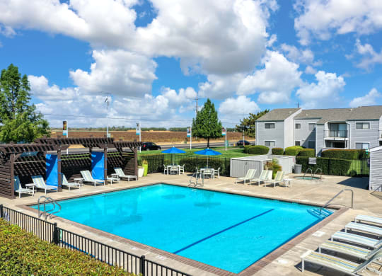 Community Swimming pool from a distance showing the entire pool, lounge chairs, cabana areas and apartment homes in the background.  Blue skies with large fluffy clouds at Silverstone Apartments, Davi