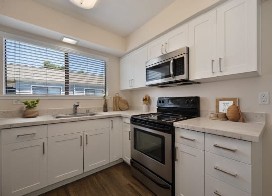 a kitchen with white cabinets and black appliances and a window at Silverstone Apartments, Davis