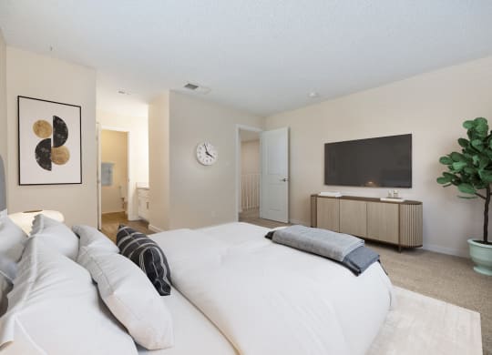 Primary bedroom in the townhouse floor plan with white bed console table and tv on the wall at Silverstone Apartments, Davis, CA