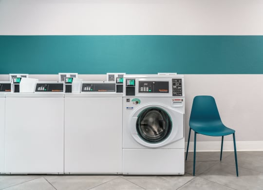 a row of washing machines in a laundry room with a blue chair