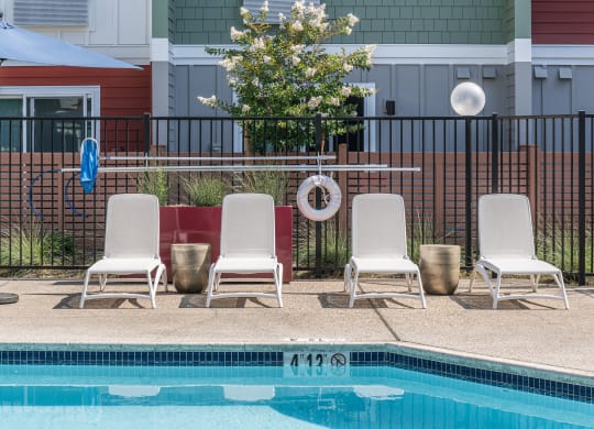 a swimming pool with three white chairs and a poolside umbrella
