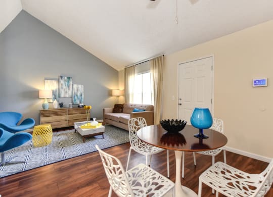 Living Room with View of Kitchen with Hardwood Inspired Floor, White Sofa, Rug and Blue Chairs at Vineyard Terrace Apartments, Napa, California