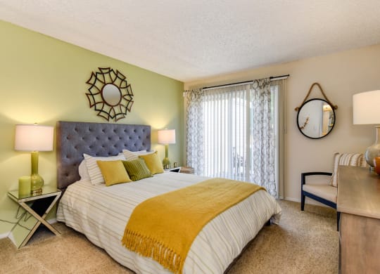 Model home bedroom with queen size bed, carpeting, nightstands and dresser with patio door on one side of room at Vineyard Terrace Apartments, Napa, CA, 94558