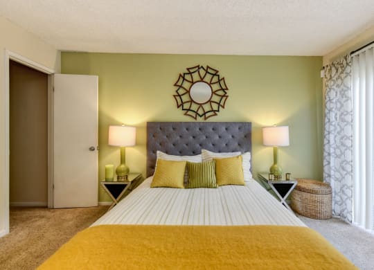 Bedroom with Carpet, light green accent Wall, two nightstands and yellow throw blanket on the bed at Vineyard Terrace Apartments, Napa