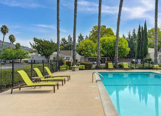 A pool surrounded by palm trees and lounge chairs at Vineyard Terrace Apartments, California