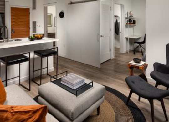 A modern living room with a grey ottoman and a black chair.