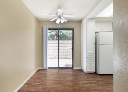 an empty living room with a white refrigerator and a ceiling fan