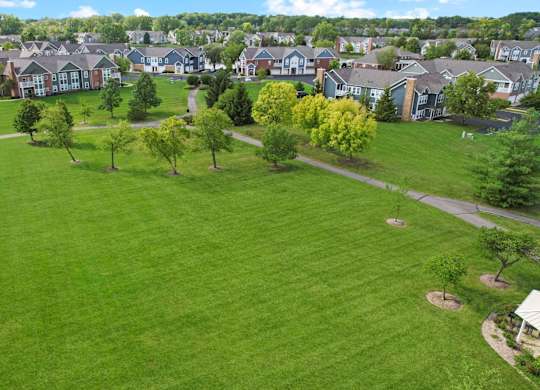 A large grassy field with trees and houses in the background.