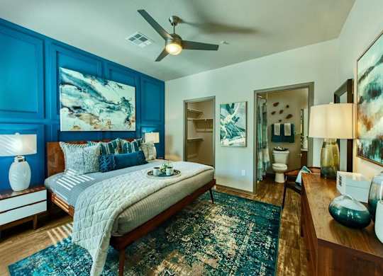 master bedroom with queen size bed and blue accent colored wall behind it. A door leads to the master bathroom and a second door shows the walk-in closet at Craft at Gilbert and Baseline Apartments, A