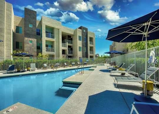Pool with buildings in the background and patio umbrella up front. Four lounge chairs line the pool. at Craft at Gilbert and Baseline Apartments, Mesa, AZ, 85204