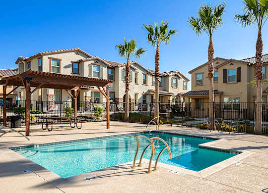 A swimming pool in front of a row of houses with palm trees.